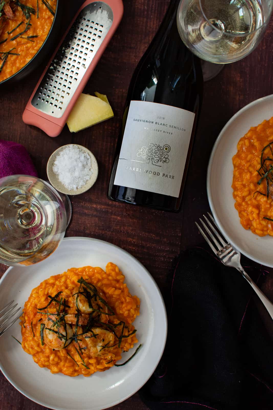 prawn risotto in a white bowl, parmesan, salt and a bottle of marri wood wine on wooden table 