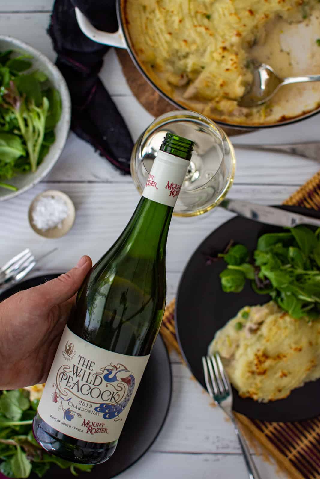 someone pouring a glass of Mount Rozier chardonny with food in the background 