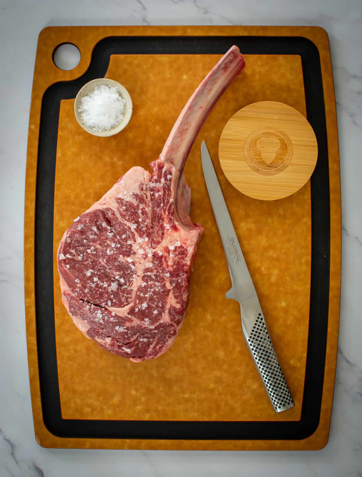 tomahawk steak, global knife and salt on chopping board 