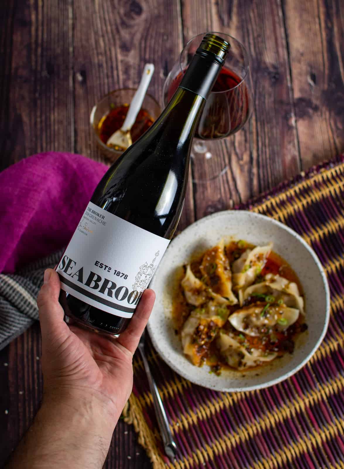 someone pouri g a glass of seabrook grenache with a bol of dumplings in the background 