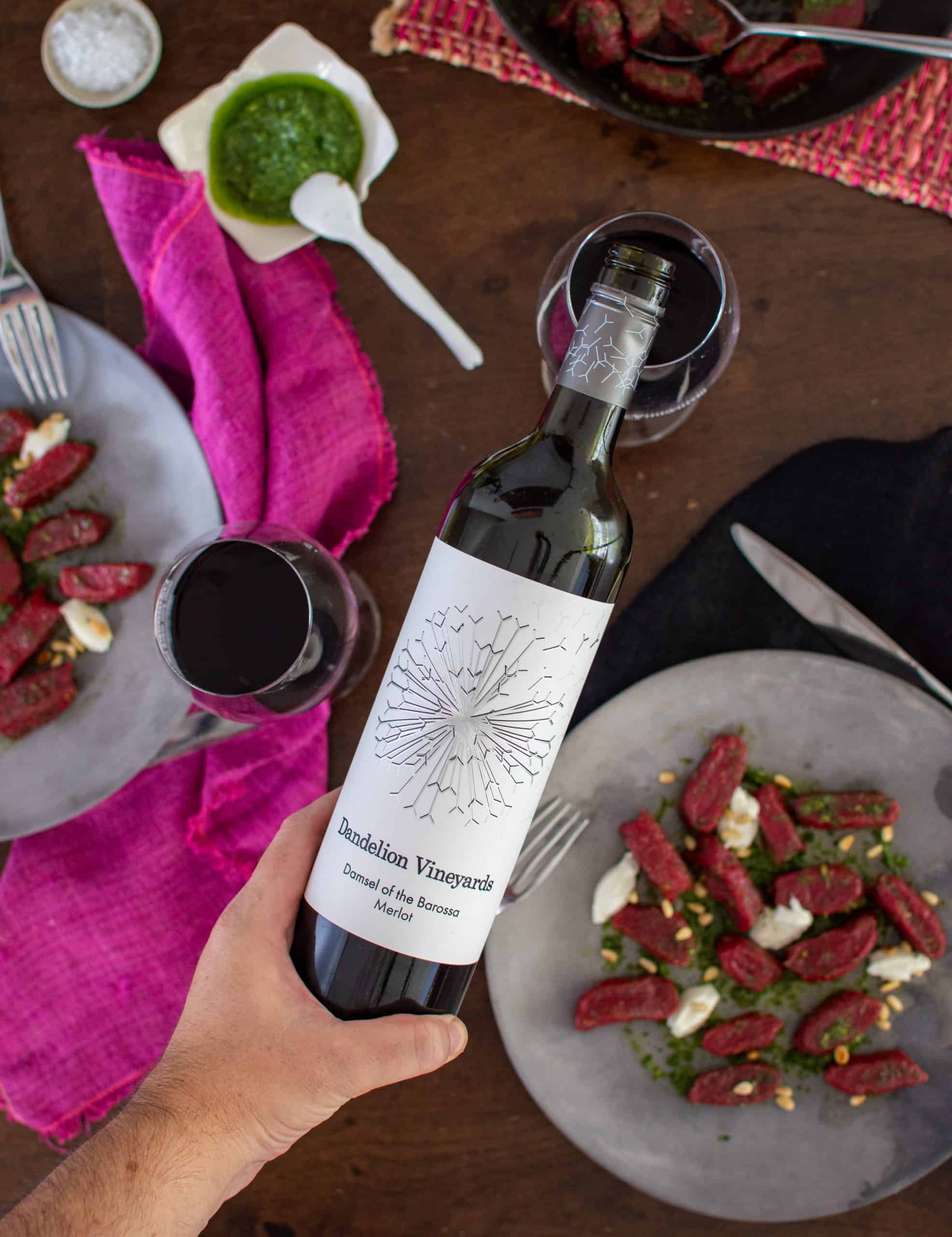Someone pouring a glass of dandelion vineyards red wine with plates of food below 