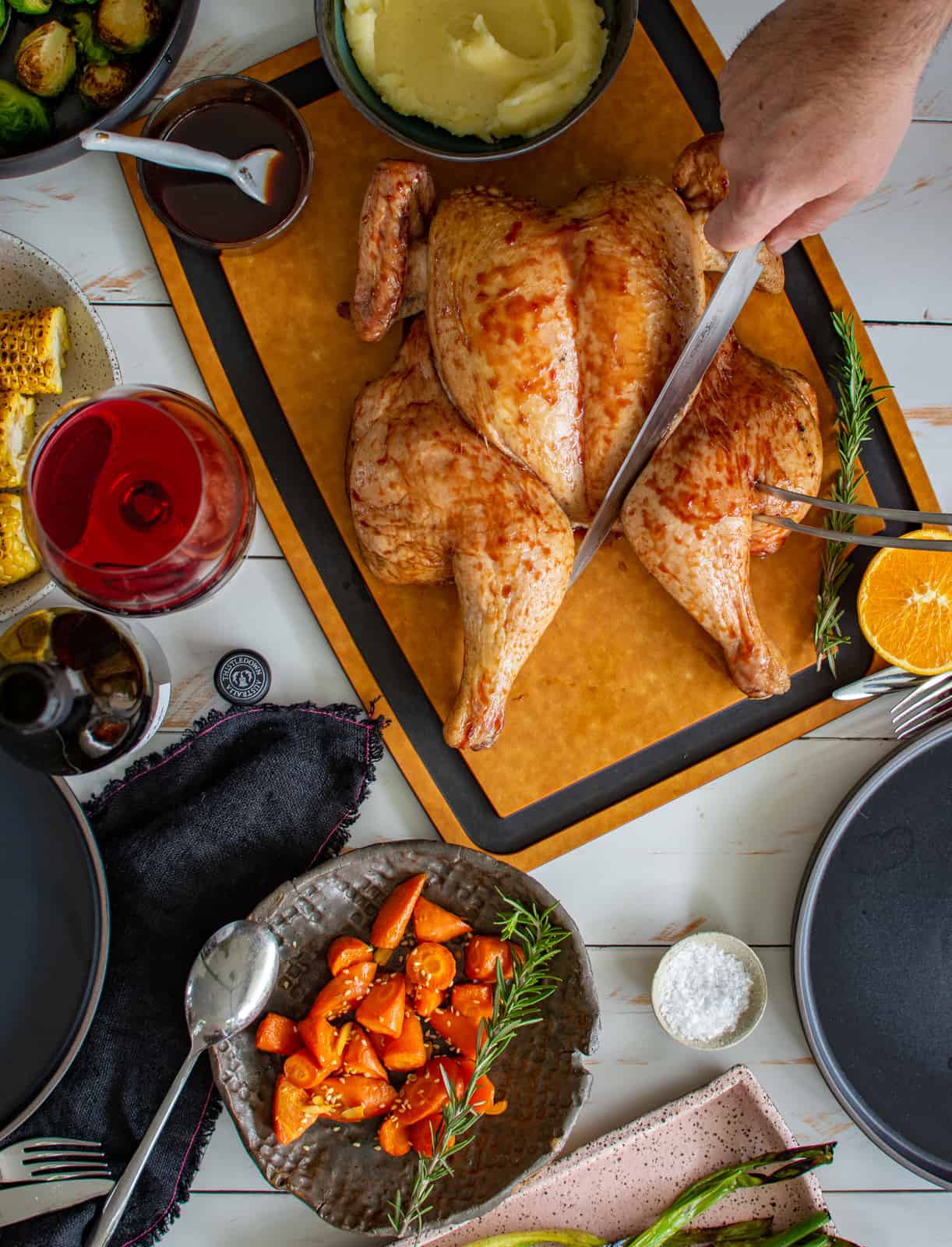 someone slicing into a smoked spatchcock chicken with bowls of vegetables in the table 