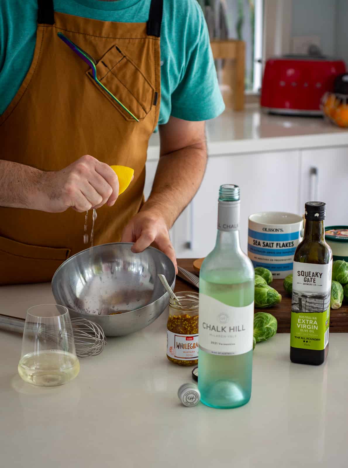 someone squeezing lemon into bowl in  a kitchen with shaved brussels sprout salad ingredients on chopping board 