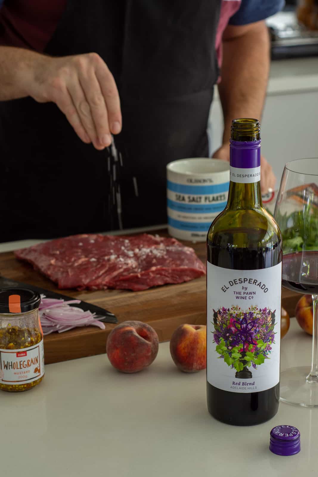 someone salting a steak on a chopping board with wine and other ingredients on counter top 