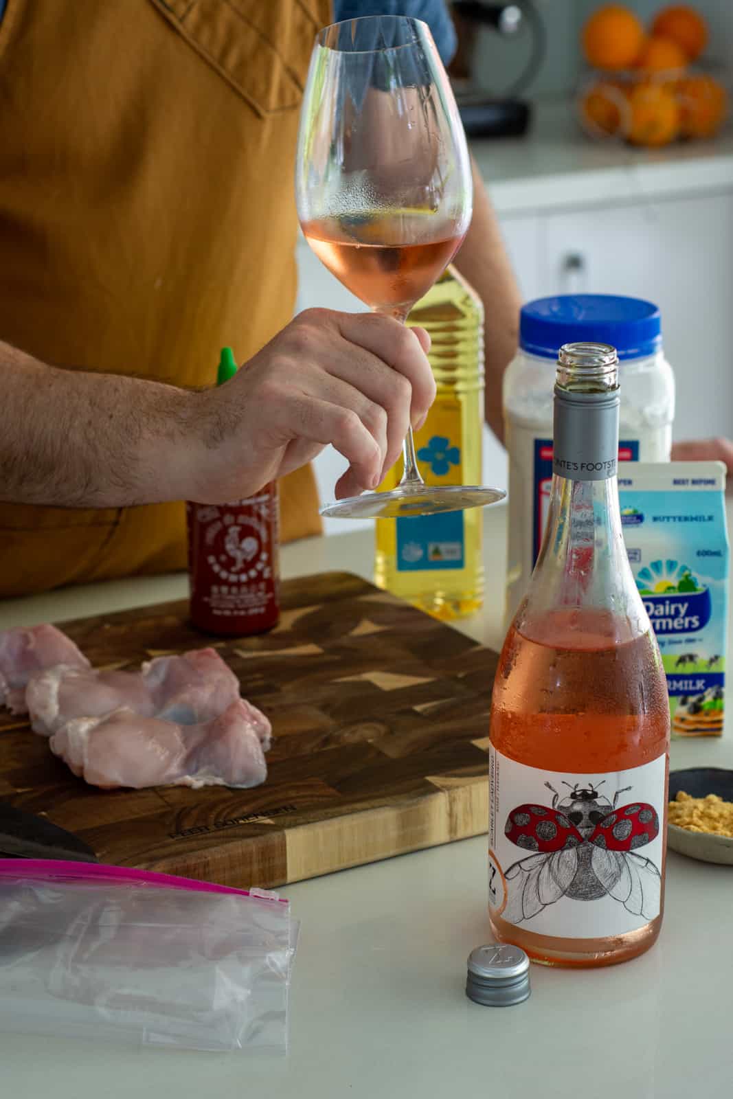 someone taking a glass of rose wine in the kitchen with chicken slider ingredients beside them 