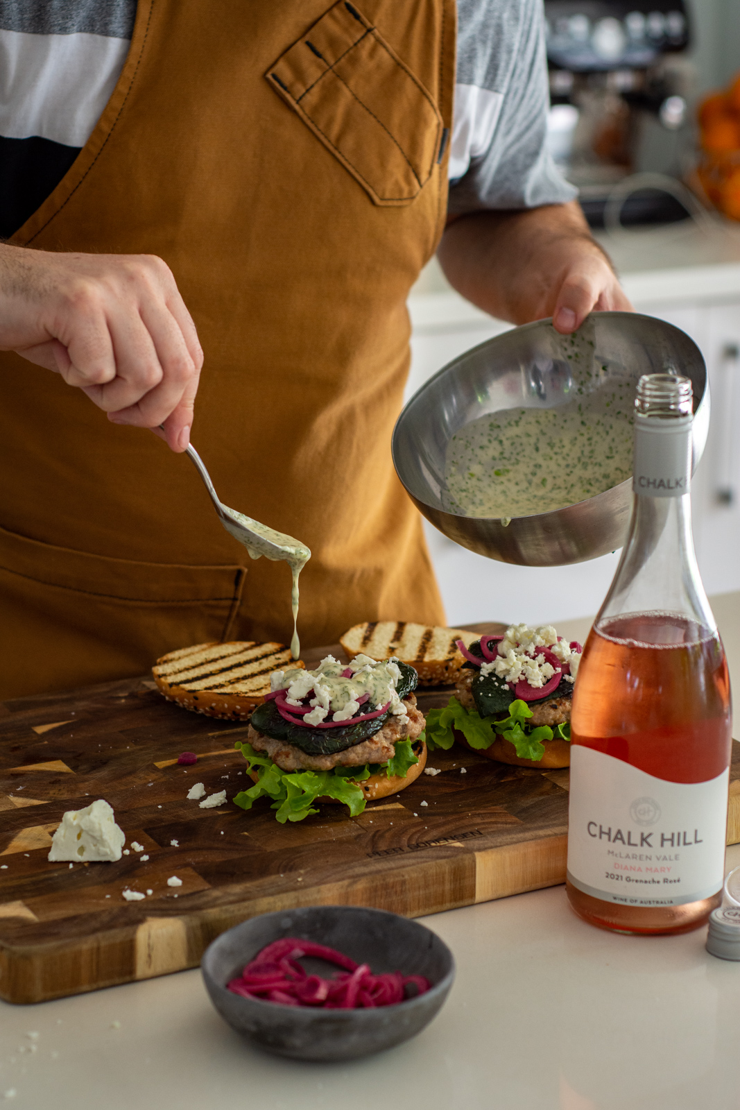 Someone assembling Mexican pork burgers in the kitchen with wine bottle next to chopping board 