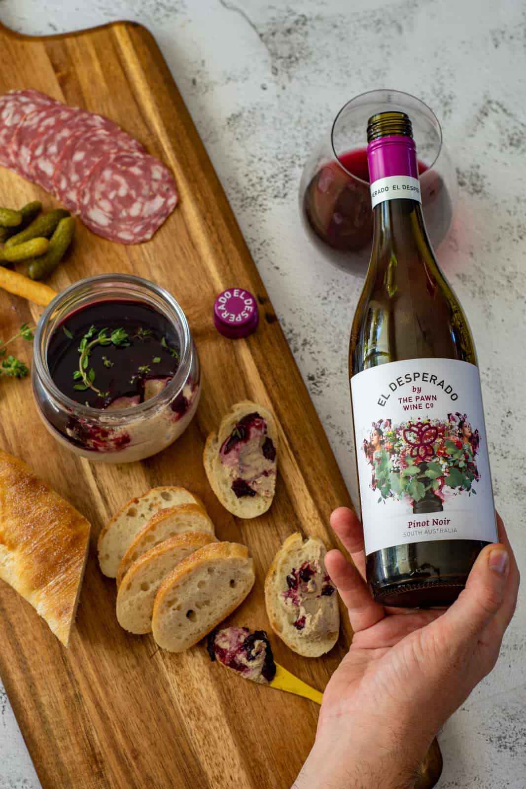 someone pouring wine into a glass with a board next to it that has mushroom pate and bread on it 