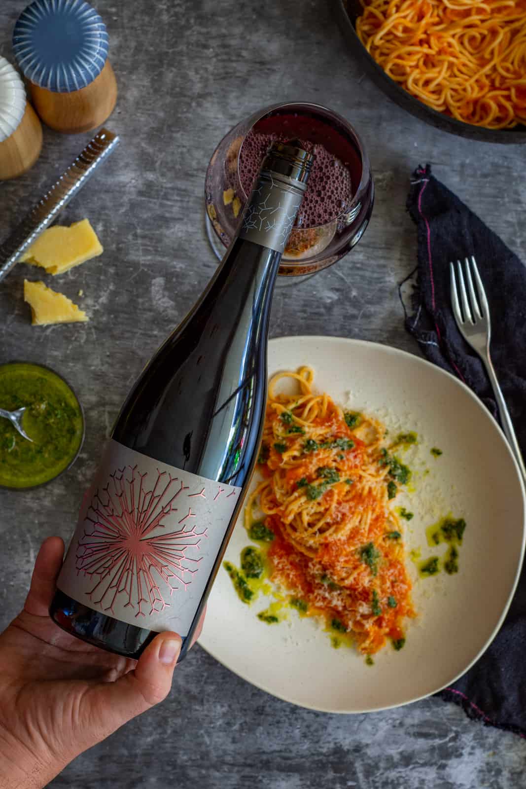someone pouring a glass of dandelion grenache wine with bowls of pasta below 