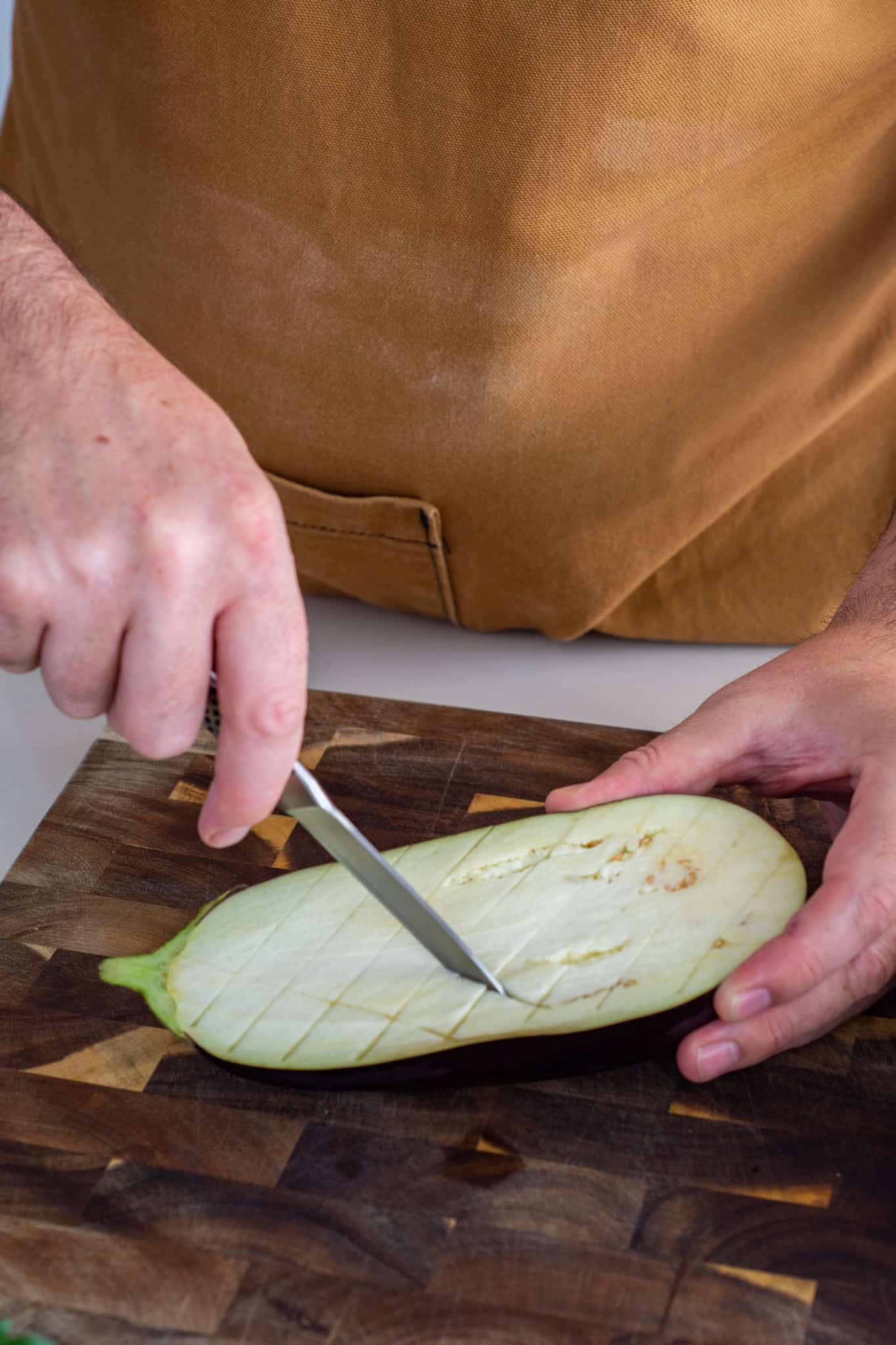 someone cutting a cross cross patterin into an aubergine 