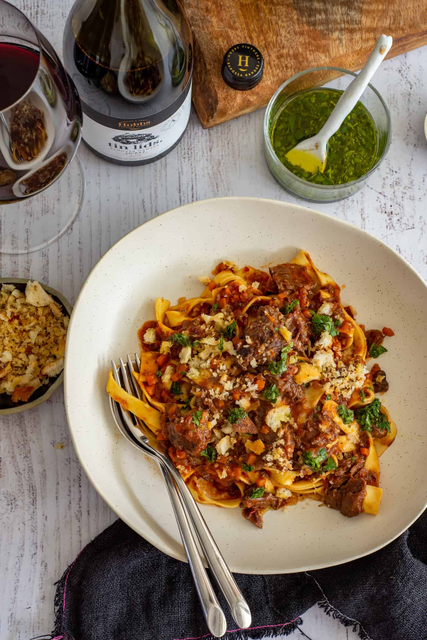 Beef cheek ragu on a plate with breadcrumbs and wine next to it
