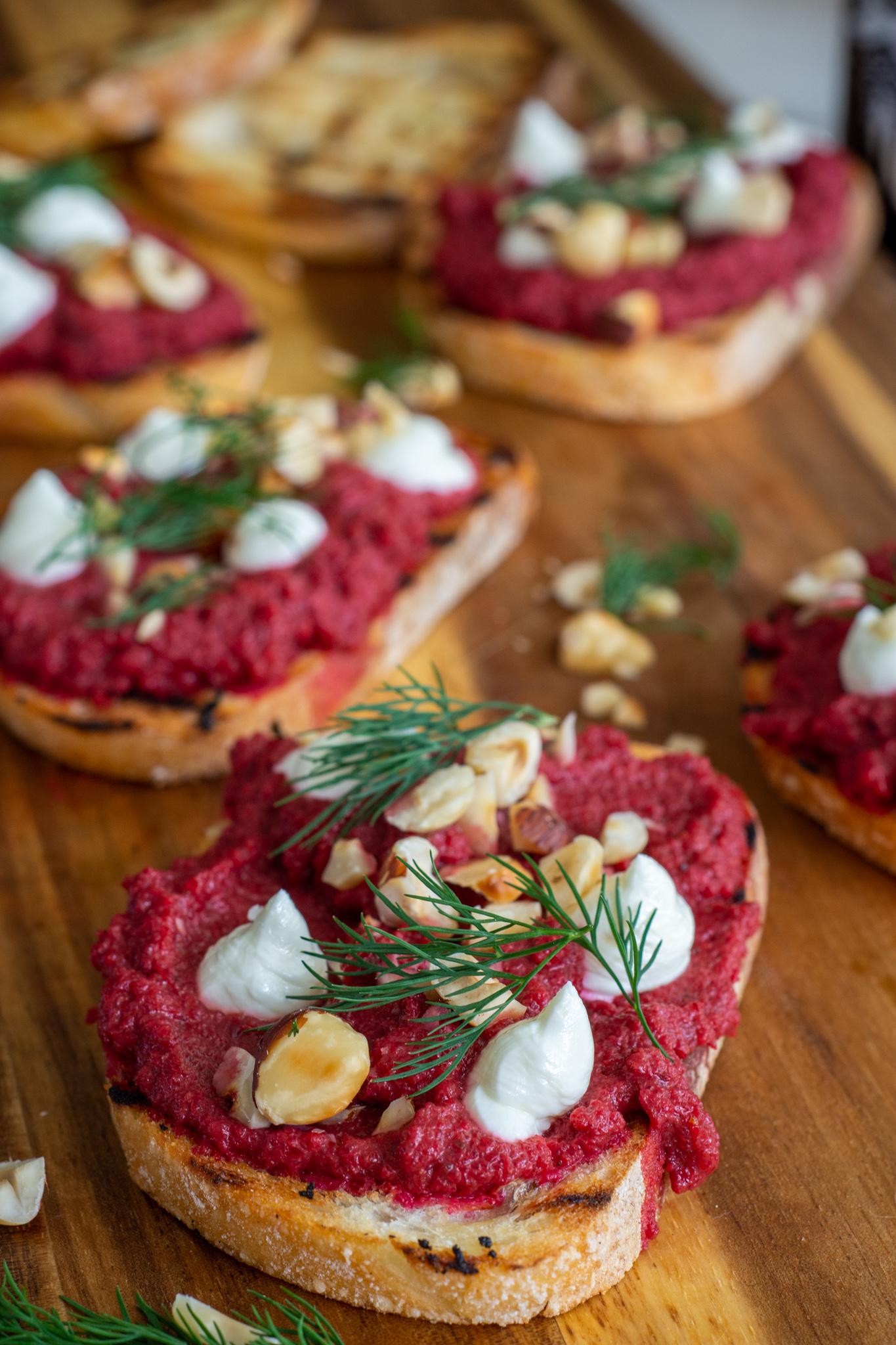 fancy toast on a chopping board.  beetroot, whipped goat cheese and hazelnuts on toast 
